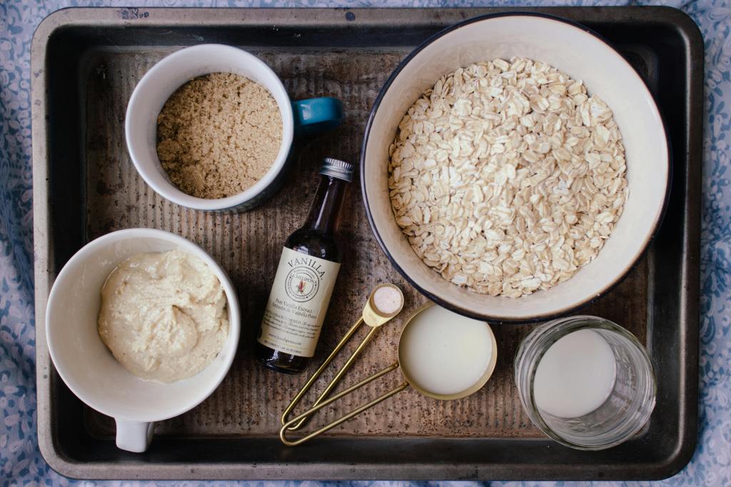 Ingredients for homemade oat milk, including rolled oats, vanilla, and brown sugar, displayed on a tray — plant-based milk alternative.