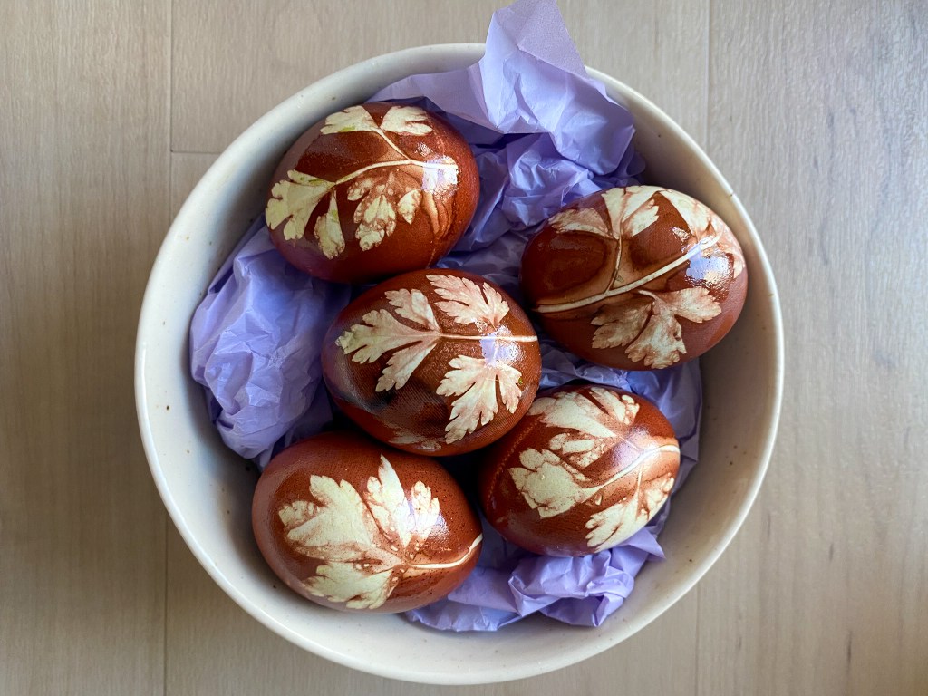 Naturally dyed Easter eggs using red onion skins and herbs, showing unique leaf patterns on each egg.